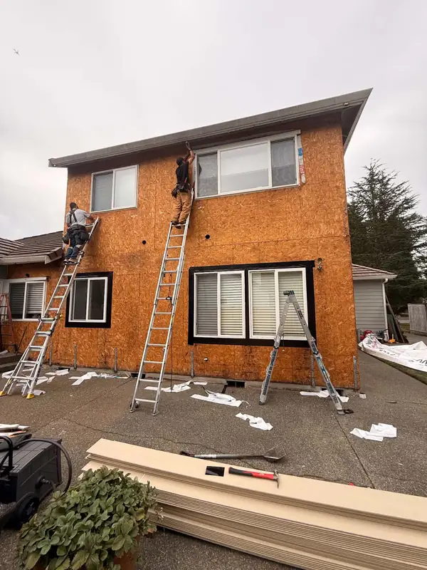 Two-story wall stripped to OSB sheathing with crew on ladders